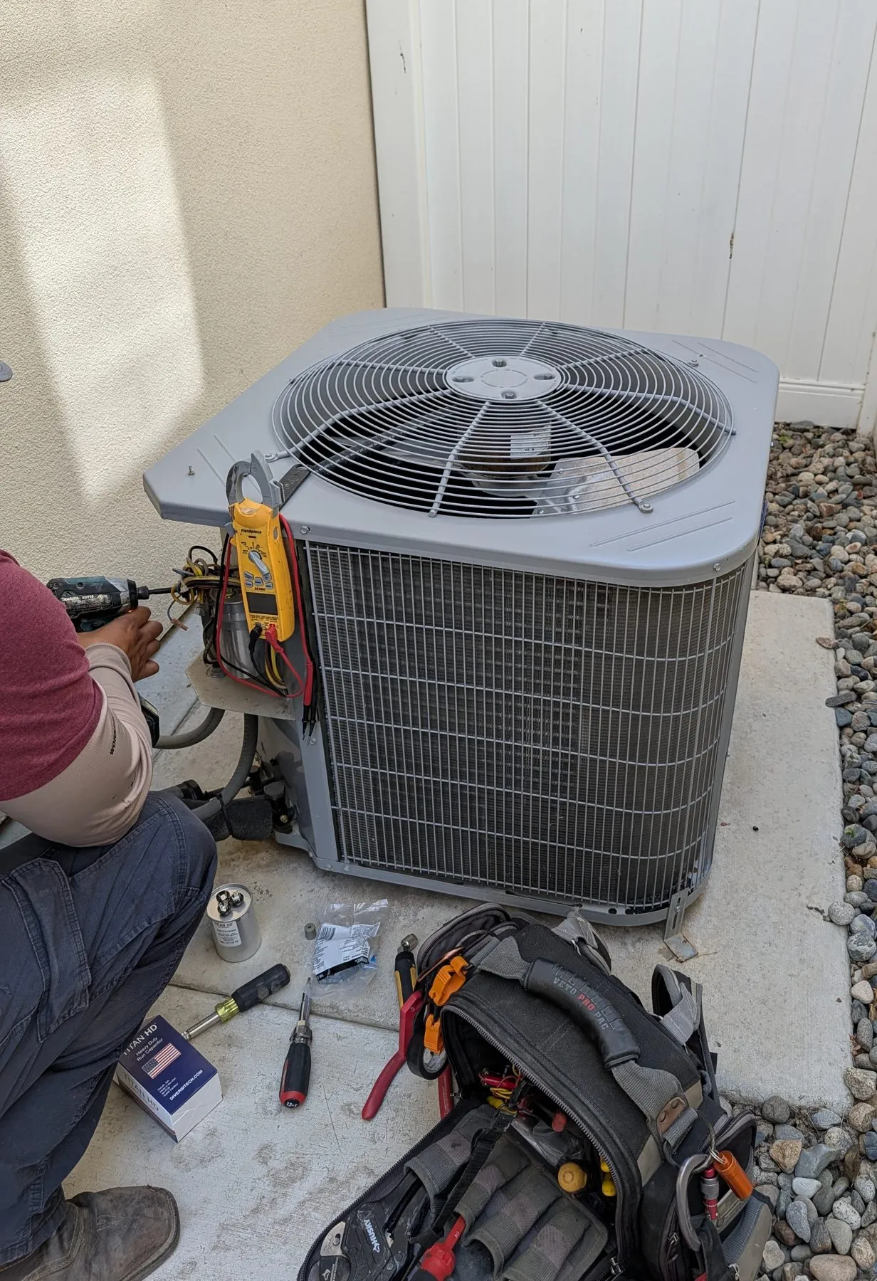 A Wildflower Climate technician replacing a failed capacitor on a Bakersfield condenser, with a clamp meter reading the circuit