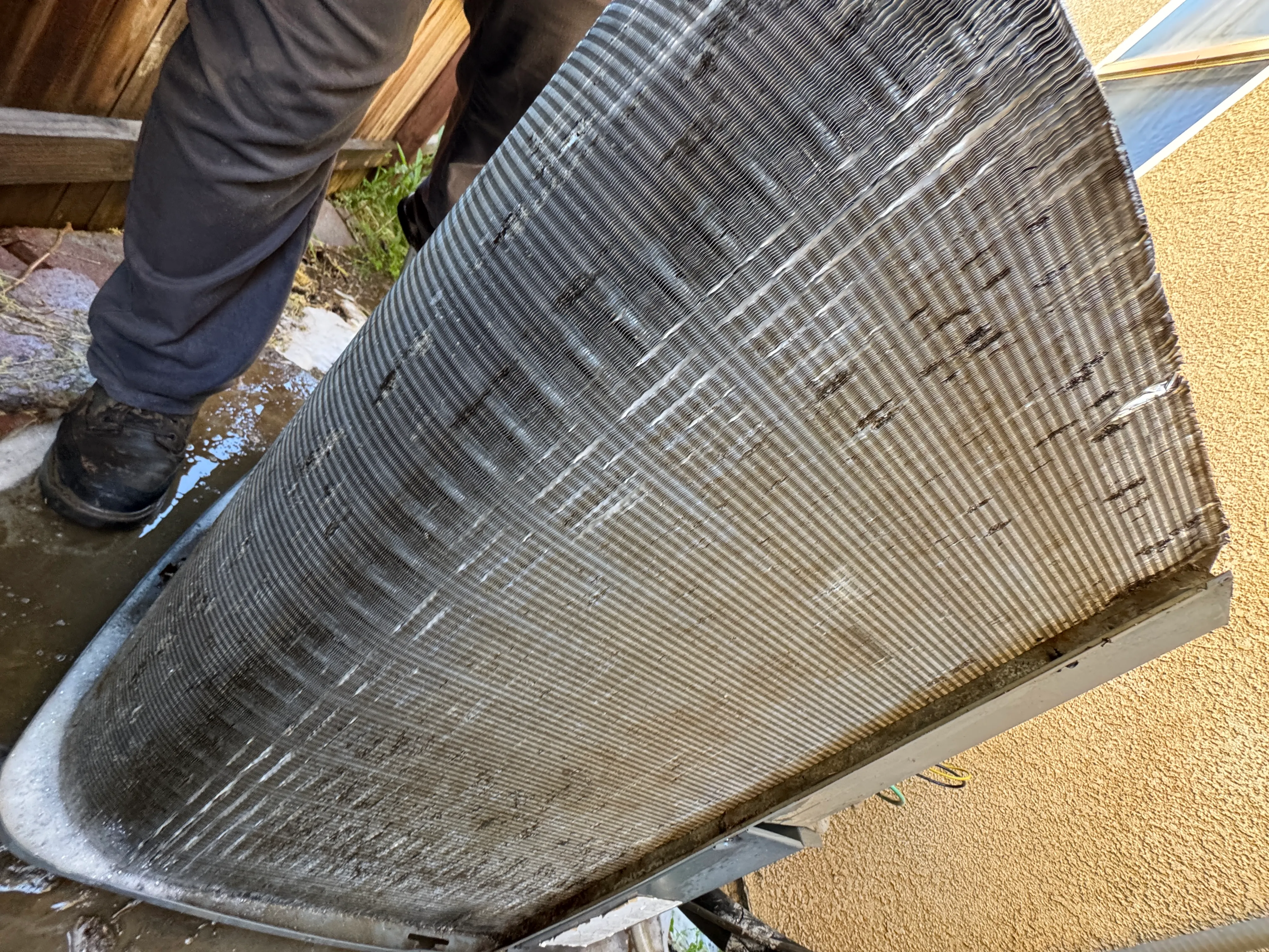 Garden hose rinse washing dust out of a condenser coil during a Comfort Reset in Bakersfield